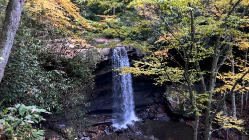 A serene waterfall cascades down rocky terrain, surrounded by vibrant autumn foliage and lush greenery.