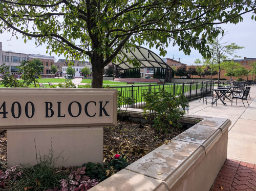 A park area with a sign reading "400 BLOCK," featuring greenery, seating, and a covered pavilion in the background.
