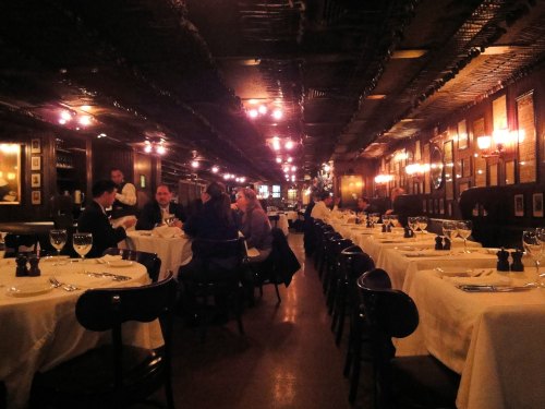 A dimly lit restaurant with white tablecloths, diners at tables, and warm lighting creating a cozy atmosphere.