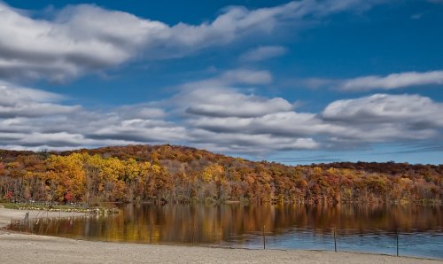 A serene lake surrounded by vibrant autumn foliage under a partly cloudy sky.