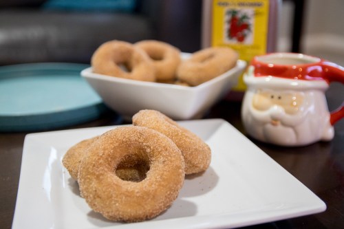 A plate of cinnamon sugar donuts with a festive Santa mug and a bowl of more donuts in the background.