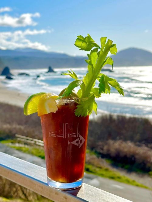A refreshing cocktail garnished with celery and lime, set against a scenic beach view.