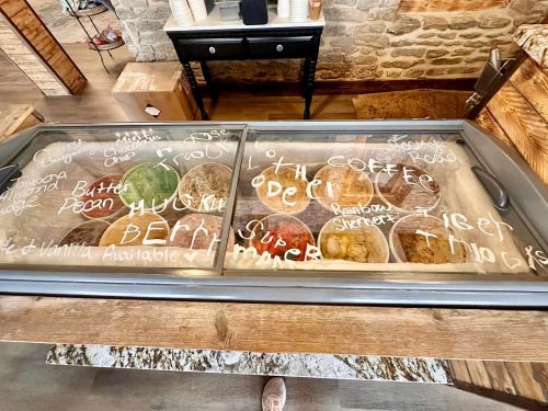 A glass display case with various ice cream flavors written in white on the surface, set in a rustic wooden environment.