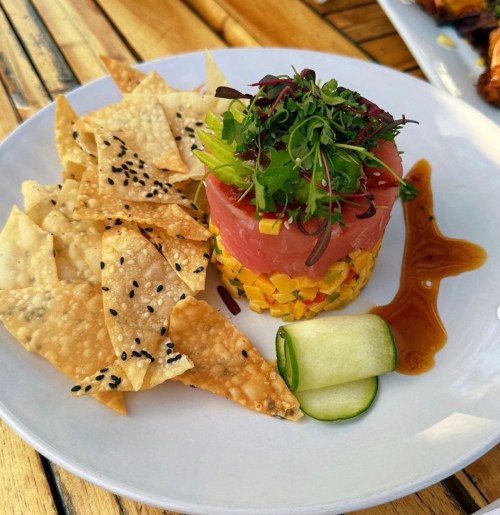 A plate featuring a colorful tuna tartare tower with mango, served with crispy chips and a drizzle of sauce.