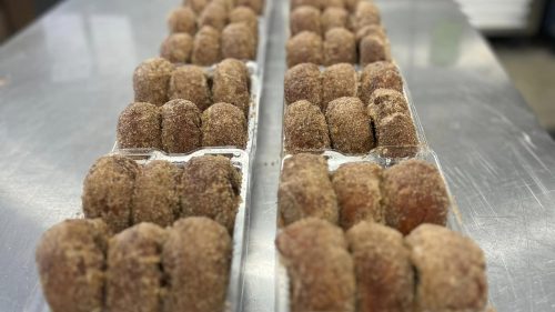 Rows of freshly made, sugar-coated doughnuts arranged in clear trays on a stainless steel surface.