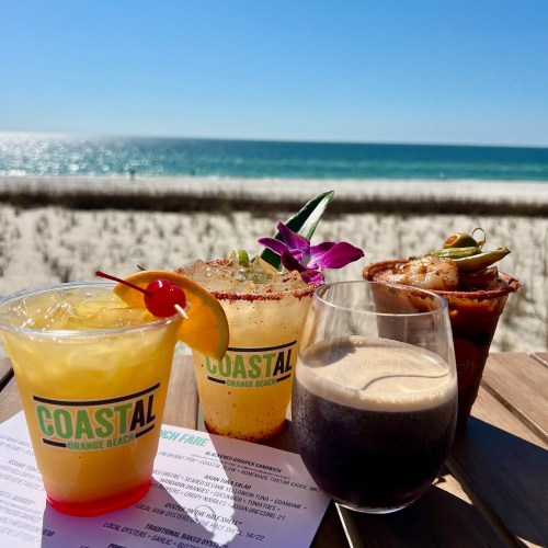 Four colorful cocktails on a table with a beach view, featuring a sunny sky and ocean in the background.
