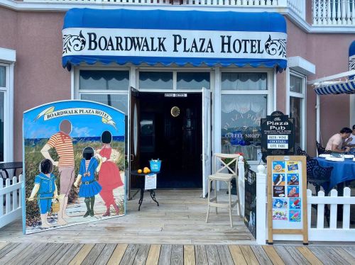 Entrance of Boardwalk Plaza Hotel with a colorful sign and outdoor seating area, featuring a coffee shop and playful artwork.