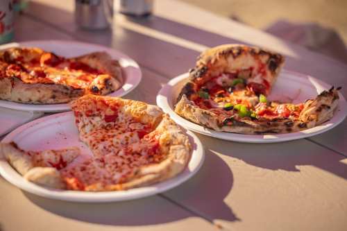Three plates of pizza on a table, featuring slices with pepperoni, cheese, and green peppers.