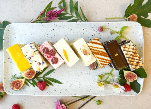A platter of colorful desserts, including various cakes and pastries, garnished with fresh flowers and figs.