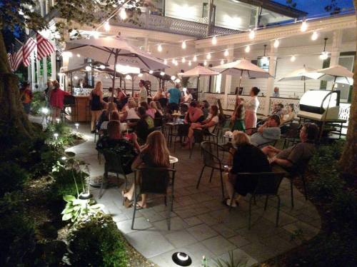 A lively outdoor dining area with string lights, umbrellas, and people enjoying their evening at a restaurant.
