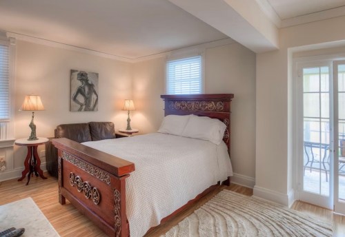 Cozy bedroom featuring a wooden bed, lamps, a leather couch, and a door leading to a balcony.