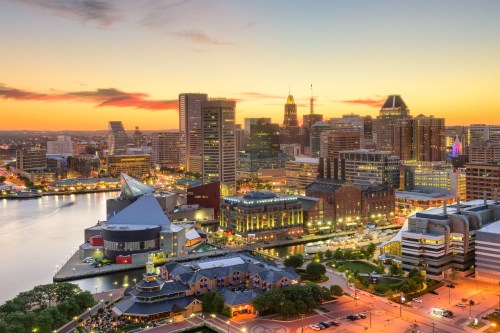 A vibrant city skyline at sunset, featuring modern buildings and a waterfront with lights reflecting on the water.