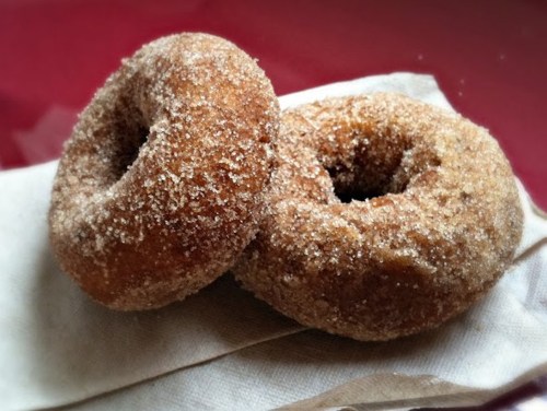 Two sugar-coated donuts on a napkin, resting on a red surface.