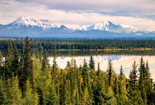 A serene landscape featuring a lake surrounded by dense forests and majestic snow-capped mountains in the background.