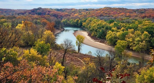 A winding river flows through a vibrant autumn landscape with colorful trees and rolling hills.