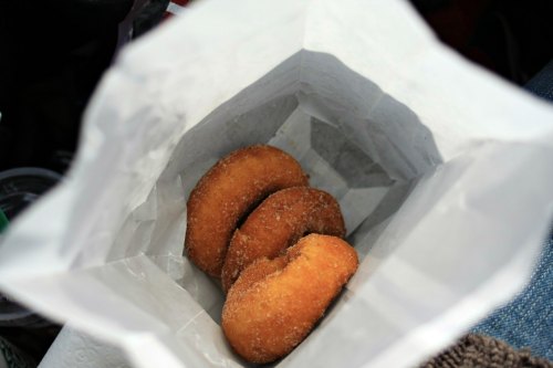 A paper bag containing three sugar-coated donuts.