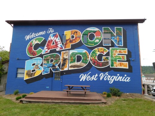 Colorful mural on a building welcoming visitors to Capon Bridge, West Virginia, with a picnic table in front.