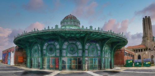 A circular, ornate green building with a domed roof, surrounded by a parking lot and dumpsters, under a cloudy sky.