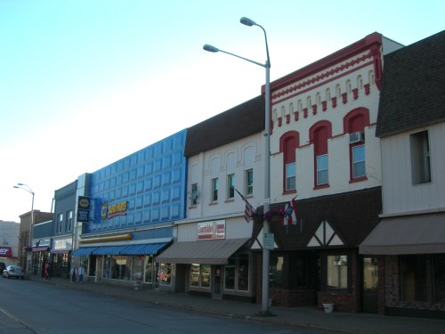 A row of colorful storefronts on a small-town street, featuring various businesses and decorative awnings.