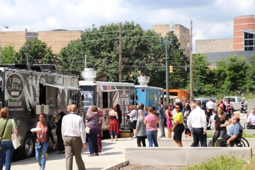 A bustling scene of people enjoying food from various food trucks in an outdoor setting.