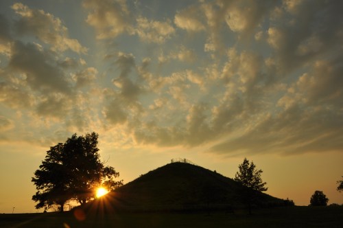 Silhouette of a shadowed hill against a blue and yellow cloudy sky at sunset.