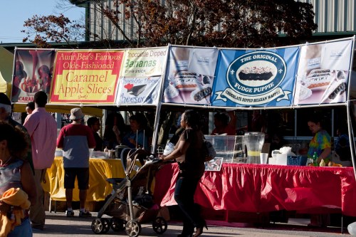 A bustling outdoor market with colorful food stalls, featuring caramel apple slices and chocolate-dipped treats.