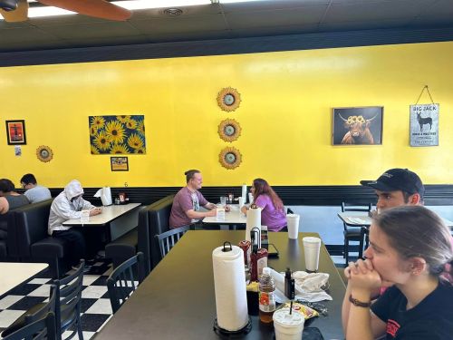A bright yellow diner interior with patrons at tables, featuring sunflower artwork and checkered flooring.