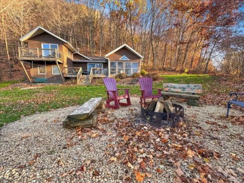 Cozy cabin surrounded by autumn foliage, featuring a fire pit and colorful chairs in a serene outdoor setting.