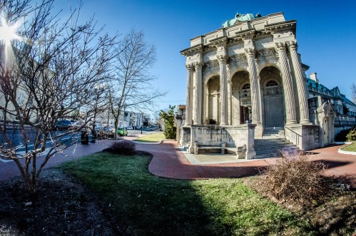 Historic building with grand columns, surrounded by trees and a clear blue sky, in a well-maintained urban area.