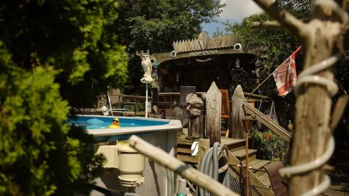 A whimsical backyard scene featuring a pool, wooden structures, and lush greenery, with a rubber duck floating in the water.