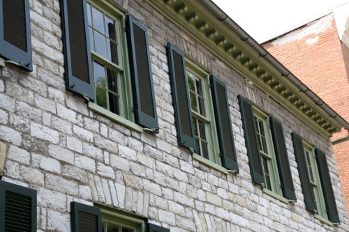 A stone building with green shutters and multiple windows, showcasing a classic architectural style.