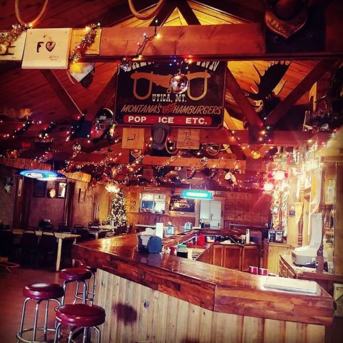 Cozy bar interior decorated with lights, a sign for hamburgers, and a festive tree in a rustic setting.
