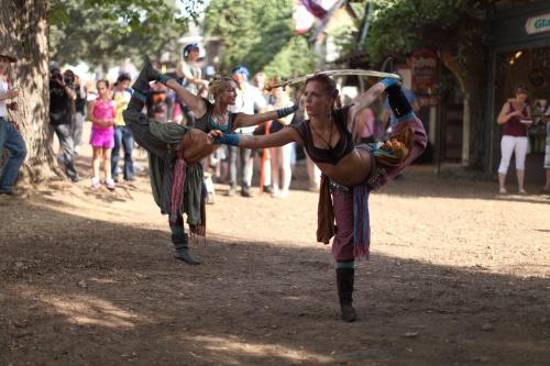 Two dancers perform a dynamic pose in a lively outdoor setting, surrounded by an audience enjoying the show.
