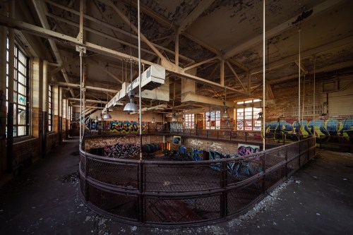 Abandoned industrial space with graffiti-covered walls and large windows, featuring a circular balcony and exposed beams.