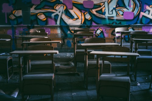 Abandoned classroom with empty wooden desks and colorful graffiti on the walls, illuminated by soft light.