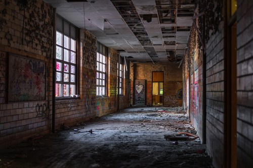 A dimly lit, abandoned hallway with graffiti on the walls and debris scattered on the floor.