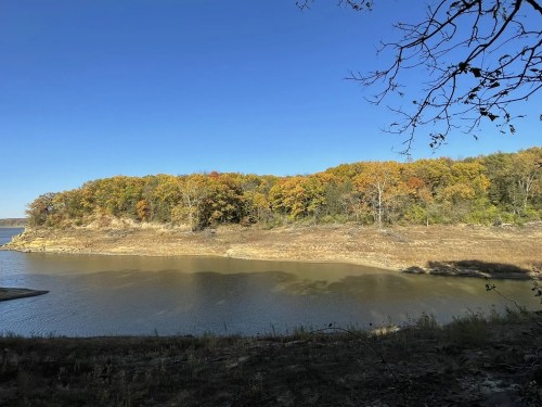 A serene landscape featuring a riverbank with autumn-colored trees under a clear blue sky.