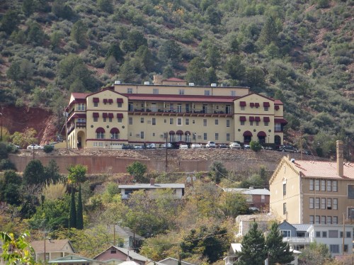 Historic building on a hillside, surrounded by trees and smaller structures, with a clear blue sky above.