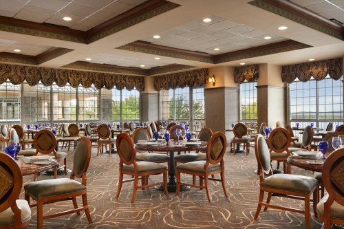 Elegant dining room with round tables, upholstered chairs, and large windows offering a view of the outdoors.
