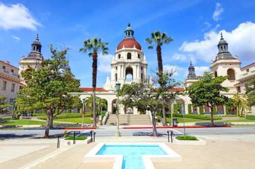 A grand building with a dome, surrounded by palm trees and greenery, under a bright blue sky.