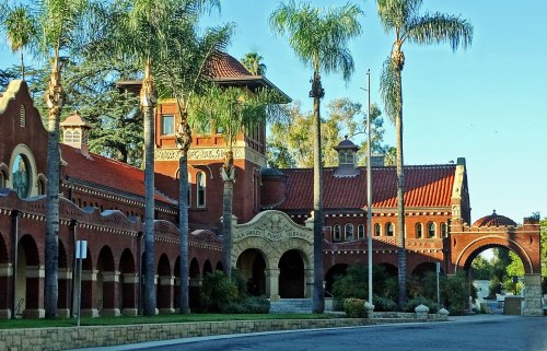 Historic brick building with palm trees, featuring arched entrances and a tower, set against a clear blue sky.