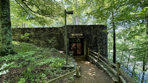 Entrance to a stone museum surrounded by lush greenery and trees, with a path leading up to the door.