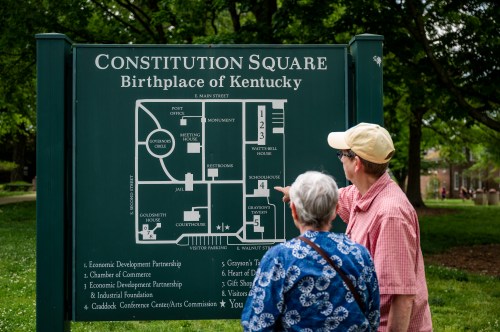 A man and woman examine a map at Constitution Square, the birthplace of Kentucky, surrounded by greenery.