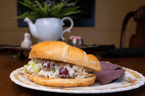 A sandwich filled with chicken salad, lettuce, and grapes, served with a side of blue corn tortilla chips.