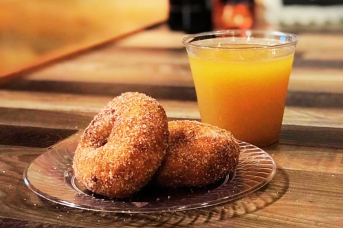 A plate with two cinnamon-sugar donuts next to a cup of orange juice on a wooden table.