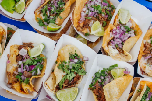 A close-up of various tacos topped with cilantro, onions, and lime wedges in white trays.
