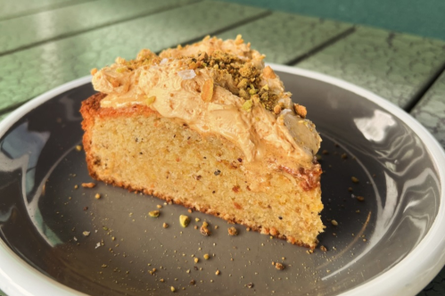 A slice of cake topped with creamy frosting and crushed nuts, served on a gray plate.