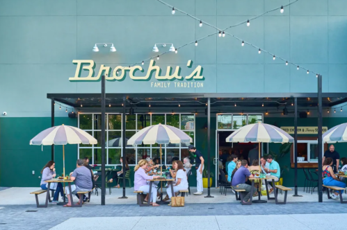 Outdoor dining scene at Brochu's, featuring patrons under striped umbrellas and a modern building facade.