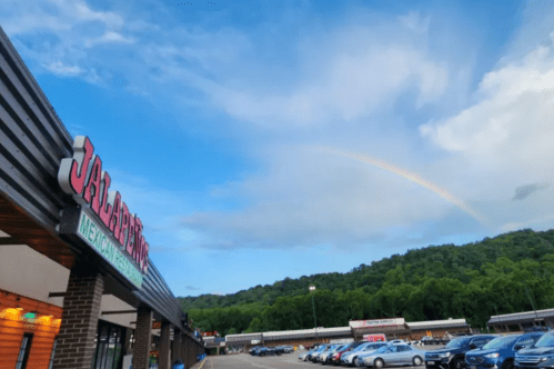 A Mexican restaurant sign with a rainbow in the sky above a shopping area surrounded by green hills.