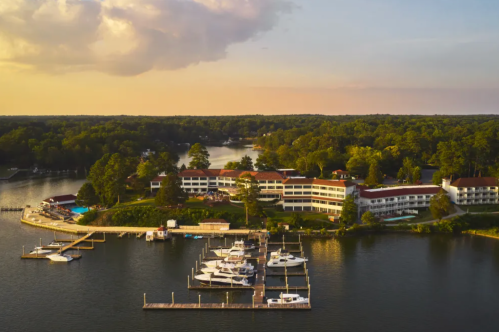 Aerial view of a lakeside resort with boats docked, surrounded by trees and a sunset sky.
